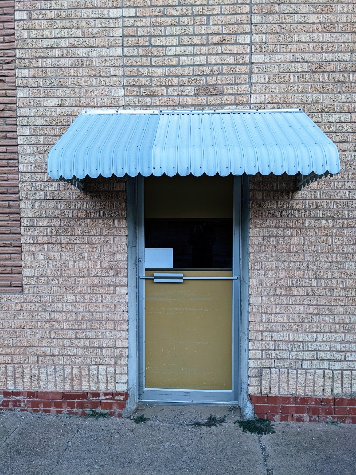 A door with a metal awning. It appears the door has not been used in some time and it's boarded up from the inside