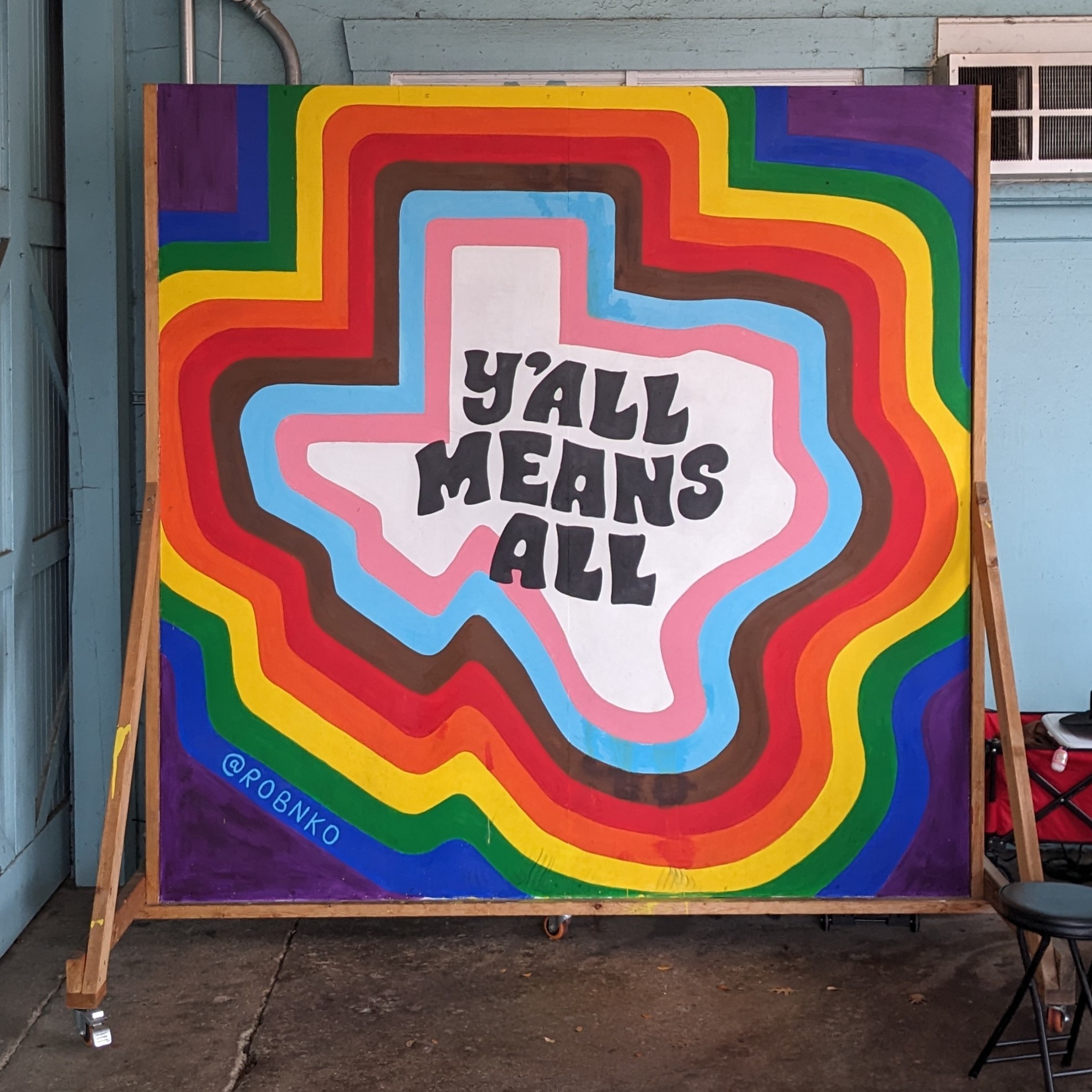 A mural of a rainbow state of TX that says "Y'all means all"