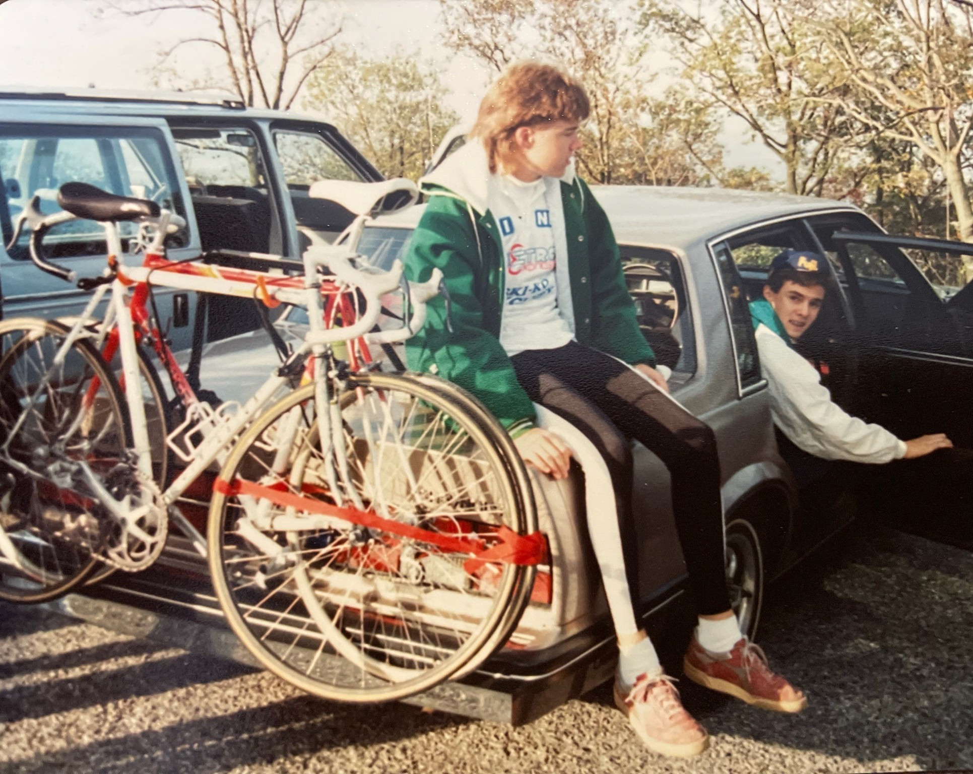 Photo c. 1990. Two boys loiter around a car before a bicycle race