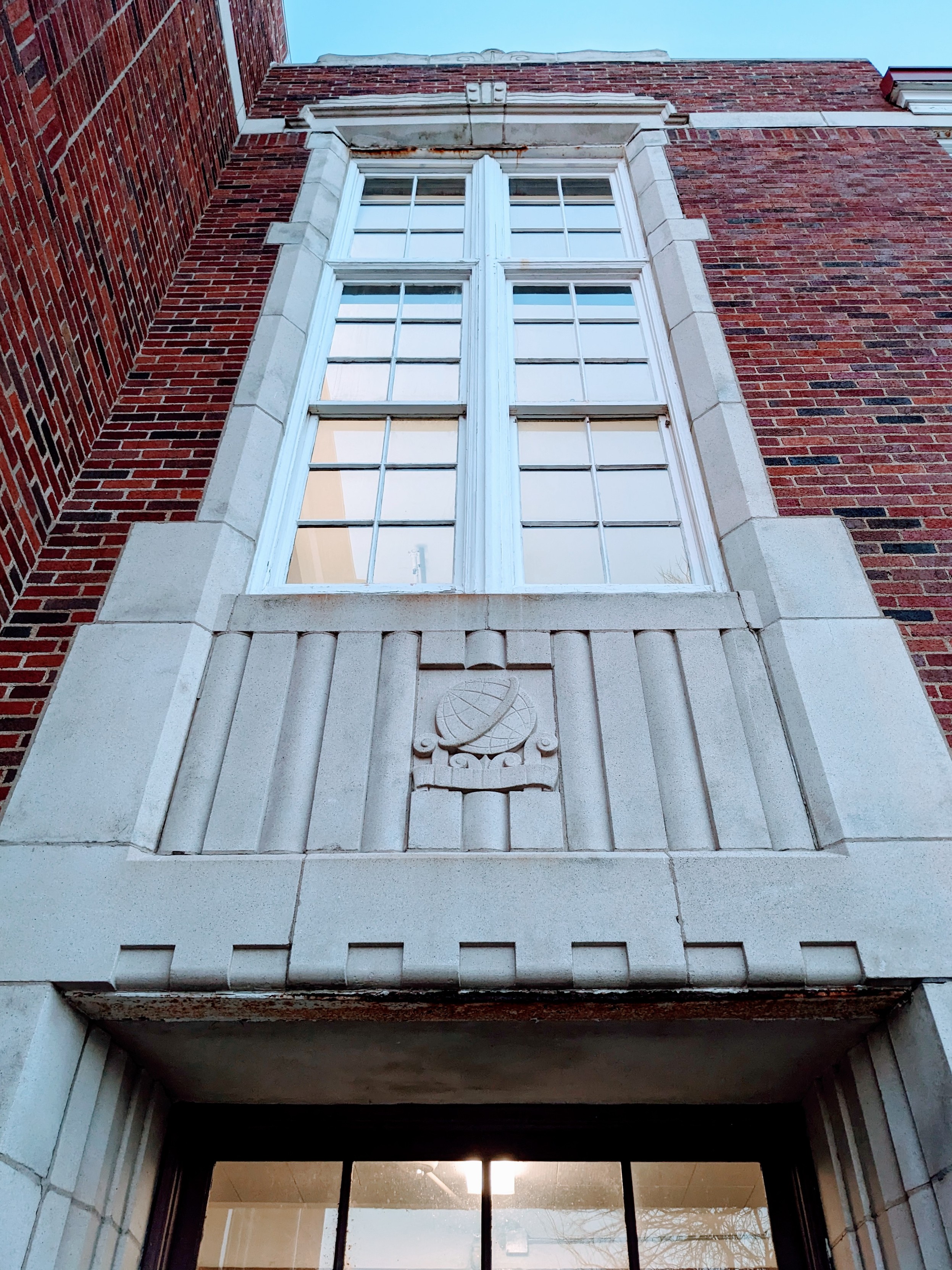 Looking up at facade of a school building built in 1933. Stone and brick, with large windows on the 2nd story 