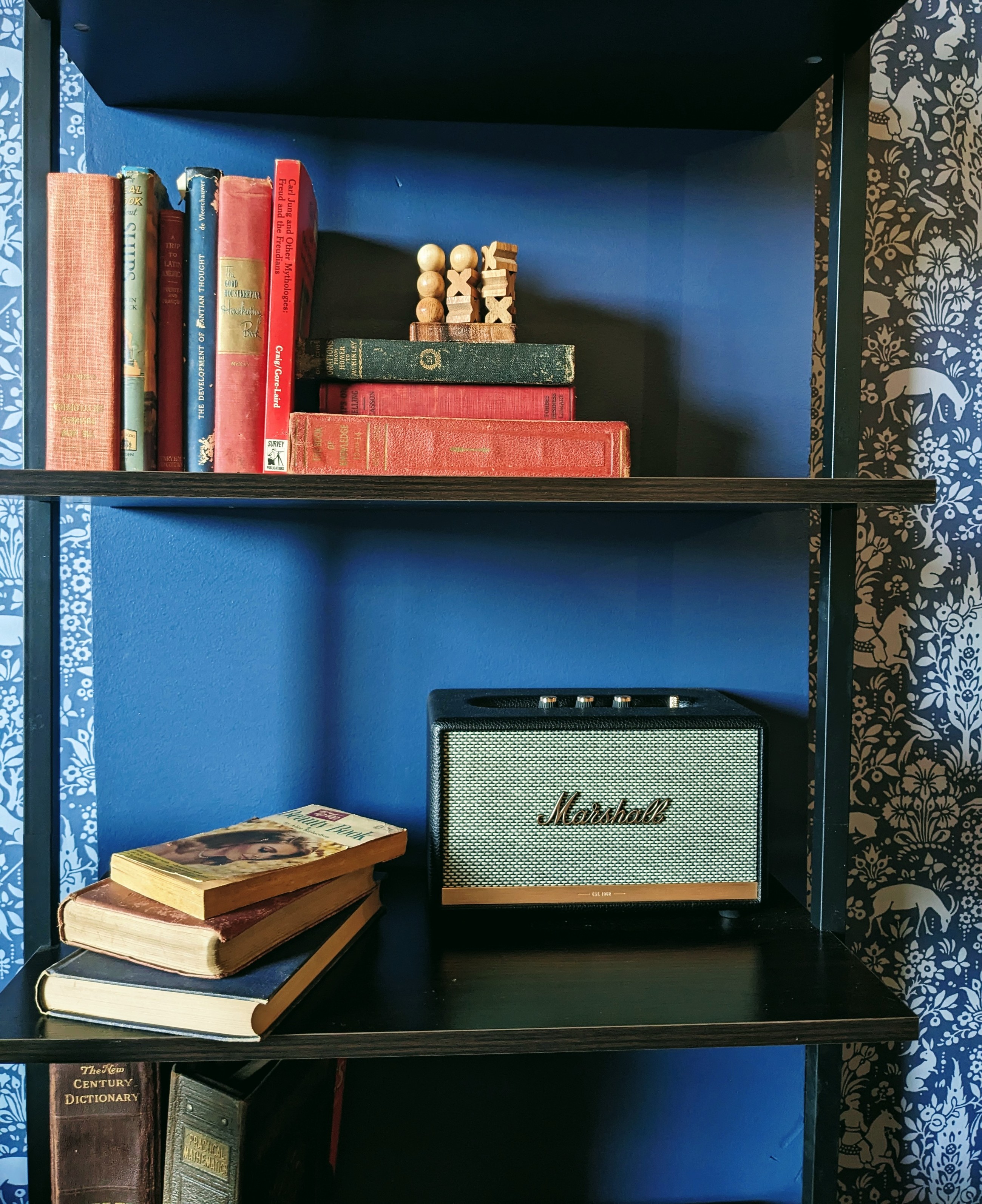 A bookshelf (in a coffee shop) with old books and a small speaker made to look like a Marshall amp 