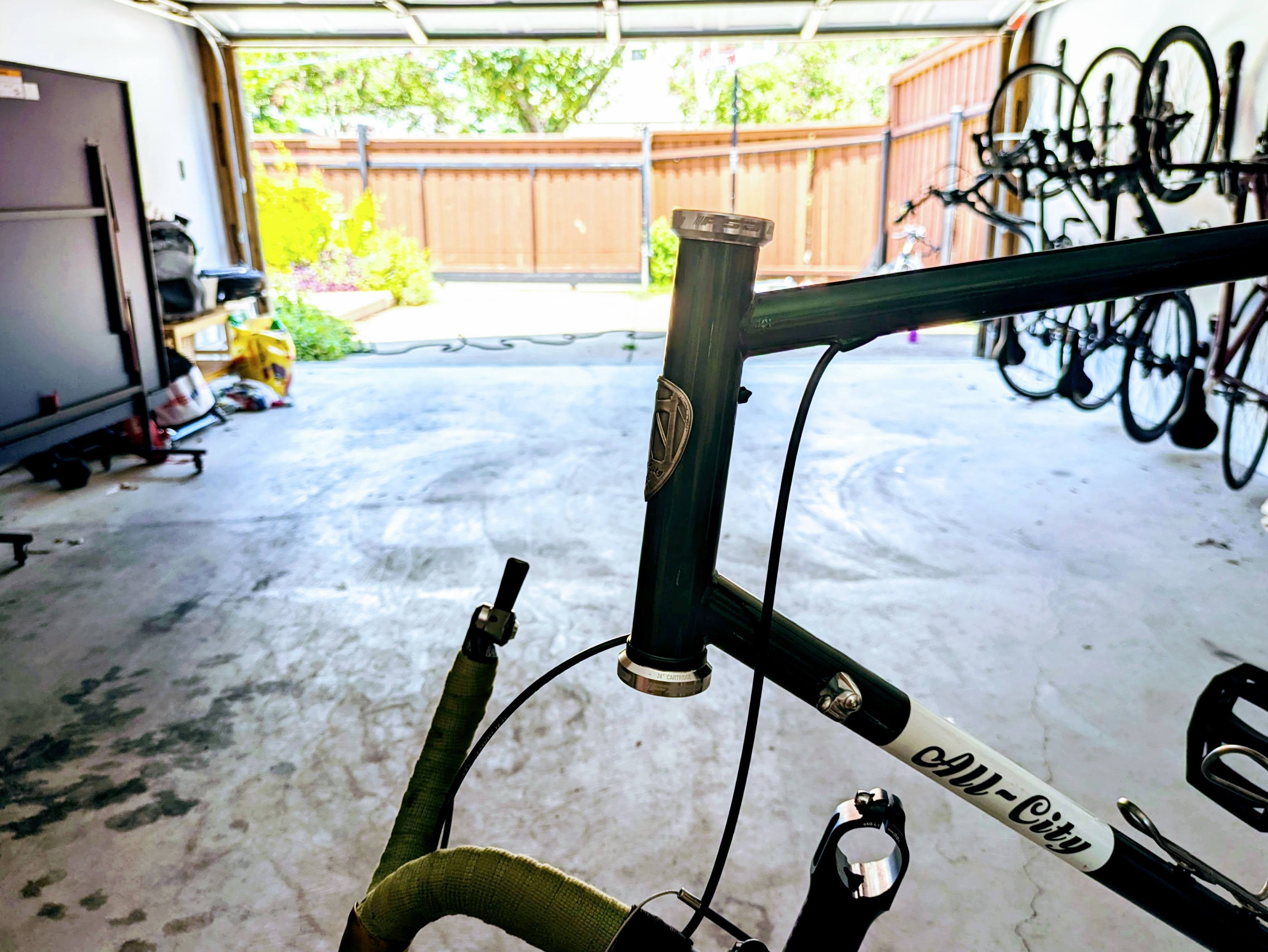 The front portion of an All-City bicycle with the fork missing and handlebars hanging by the cables