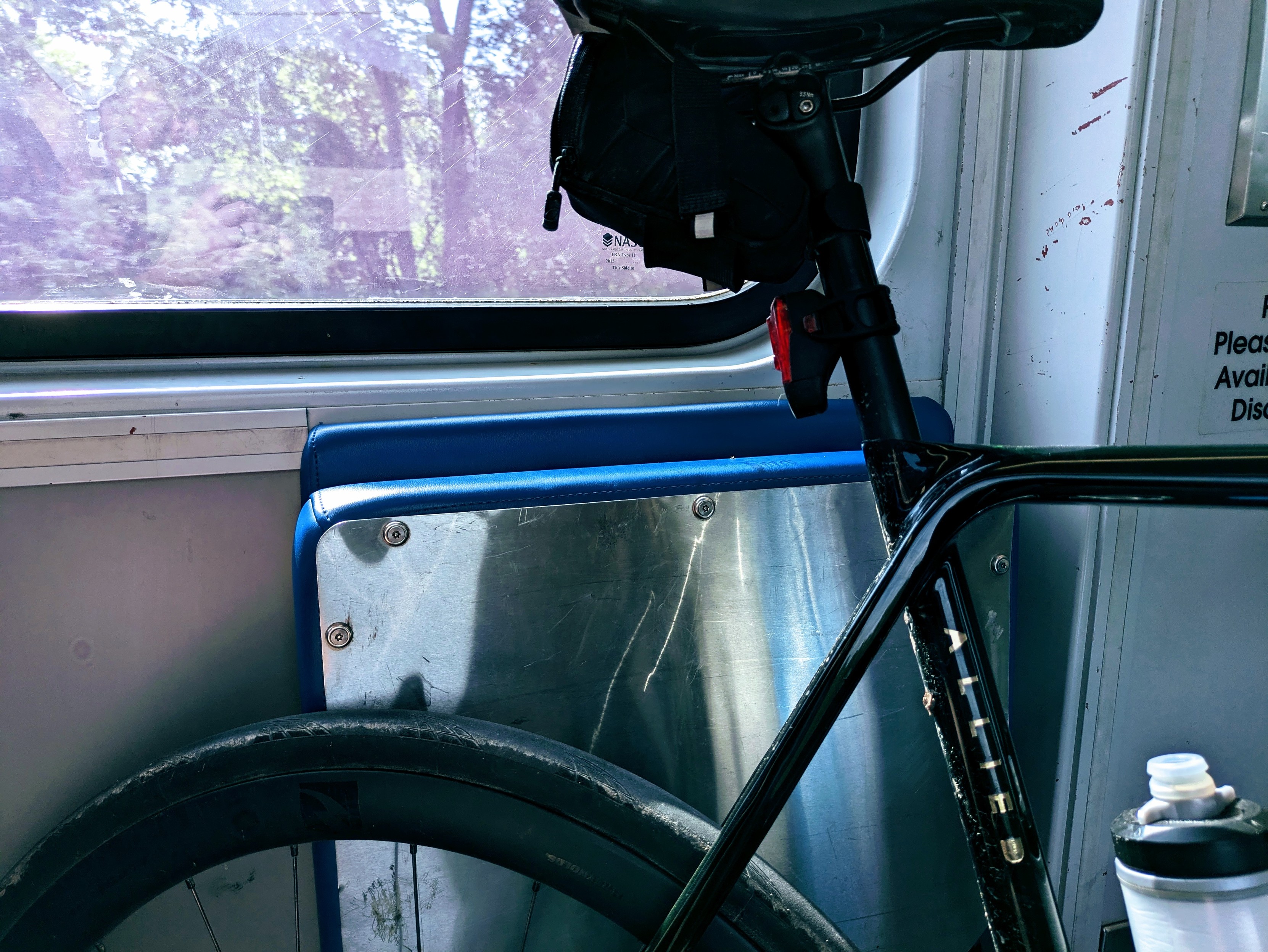 A tight cropped photo of the back 1/4 of a green Allied bicycle on a light rail carriage. The window behind the bike looks out at some trees