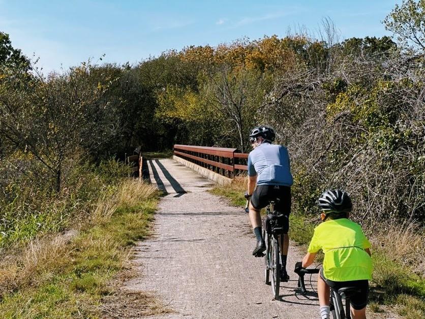A man and a boy riding bikes on a gravel trail, a bridge is ahead of them