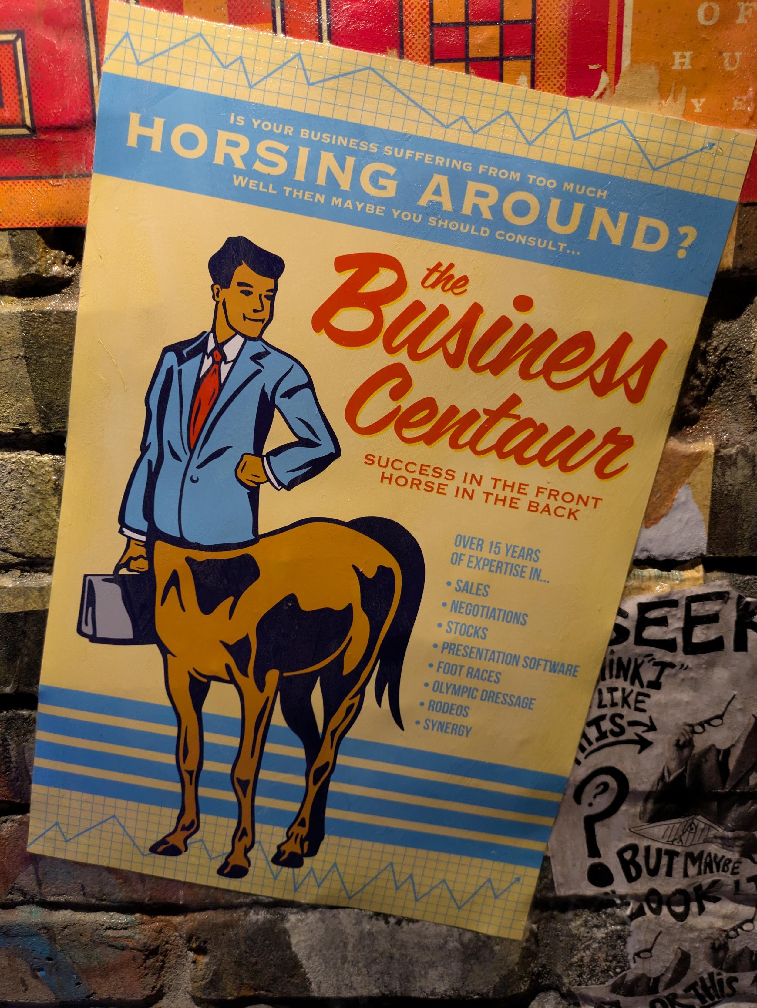 poster featuring a centaur in a business suit carrying a briefcase. The text on the poster reads:

"Is your business suffering from too much horsing around? Well then maybe you should consult... The Business Centaur. Success in the front, horse in the back." Below this, it lists "over 15 years of expertise in...":

Sales
Negotiations
Stocks
Presentation software
Foot races
Olympic dressage
Rodeos
Synergy