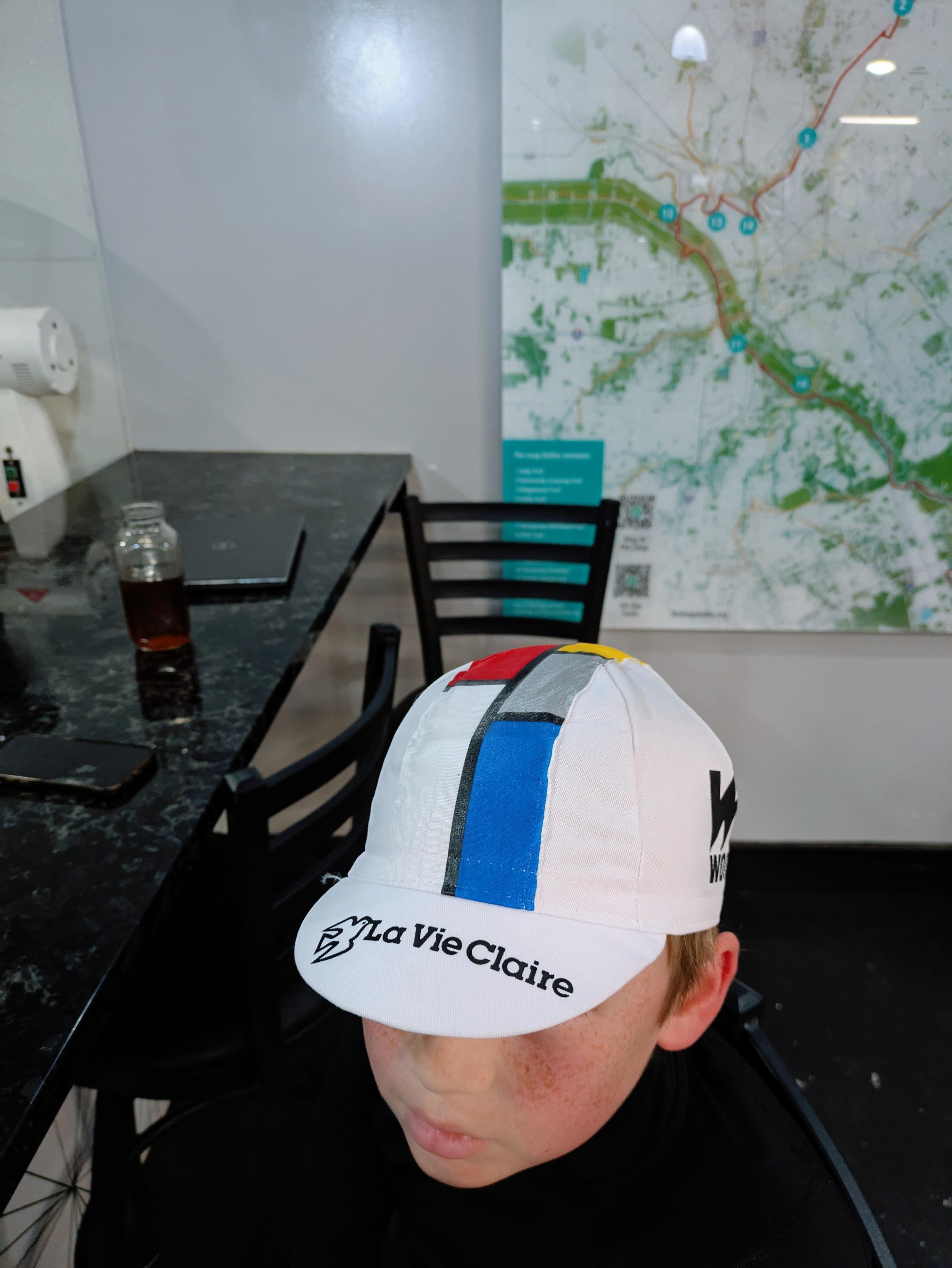 Boy in a La Vie Claire bicycle cap. The cap is white with the team's pattern across the top and the logo on the top of the brim. The La Vie Claire colors (red, yellow, blue and gray) were based on the artwork of Piet Mondrian, giving them a unique appearance in the peloton during the 80s