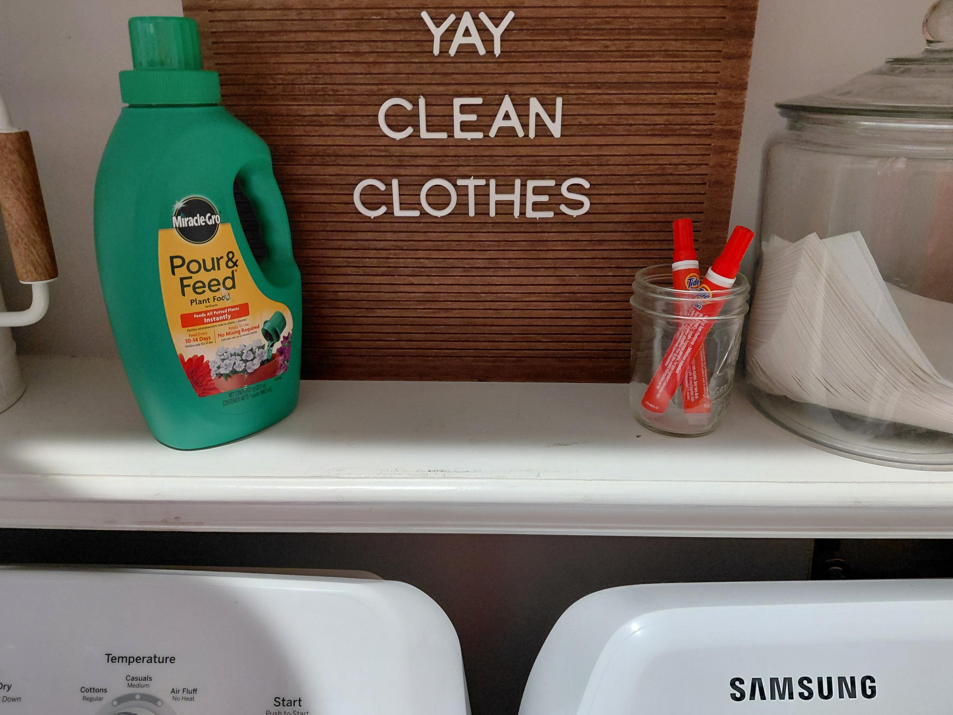 Photo of a shelf above laundry machine with a green bottle of fertilizer that looks just like a green bottle of laundry detergent 